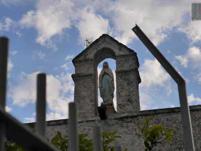 Dall�alto, incastonata in un timpano posto sul tetto, la statuina di una Madonna sembra benedire coloro che passano